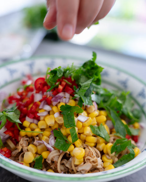 Ein bunter Teller mit Bananenblüten-Ceviche, belegt mit Mais, roten Zwiebeln, Paprika, Koriander und frischen Kräutern.