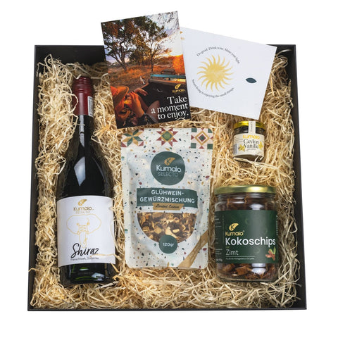 Geschenkpaket „Cozy“ mit Shiraz-Wein, Glühwein-Gewürzmischung, Kokoschips mit Zimt, Ceylon-Vanille und Karte auf Holzwolle.