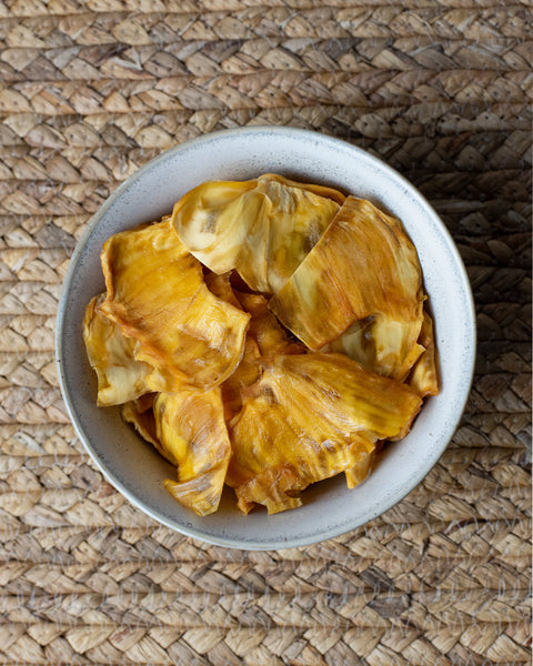 Eine Schale mit getrockneten Sweet-Jackfruit-Stücken auf einer geflochtenen Unterlage.