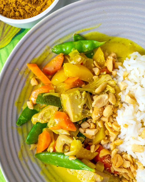 Veganes Currygericht mit Jackfruit, Gemüse, Erdnüssen und Reis in gelber Currysauce, serviert auf einem Teller.