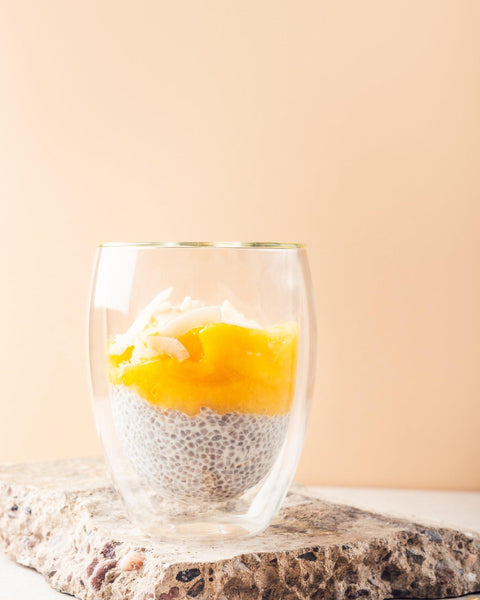 Chia-Pudding im Glas, geschichtet mit Sweet Jackfruit und Kokosraspeln, auf einem Naturstein präsentiert